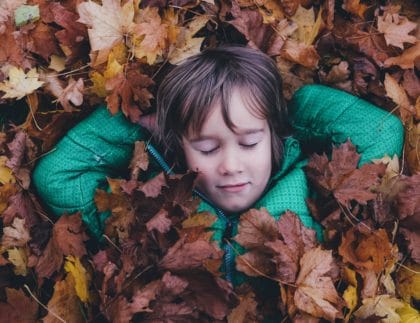 child resting in leaves outside