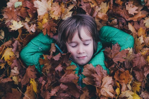 child resting in leaves outside